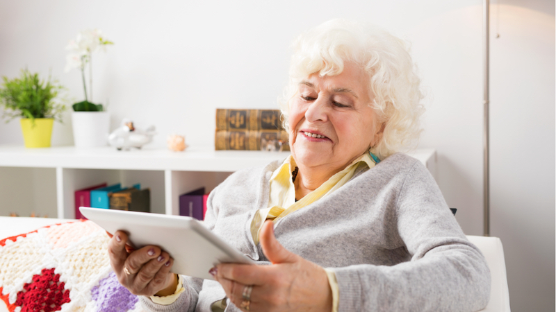 Fröhliche ältere Dame mit Tablet in der Hand: digitale Pflege kann unterschiedlich aussehen.