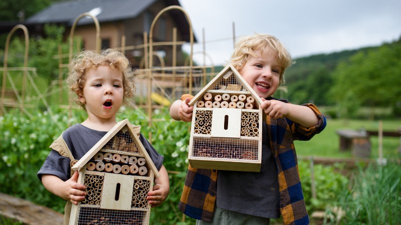 Ein kleines Mädchen und ein kleiner Junge halten stolz ein Insektenhotel in den Händen
