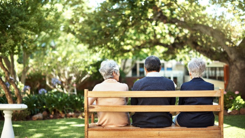 Drei Senioren sitzen auf einer Bank in einem Garten