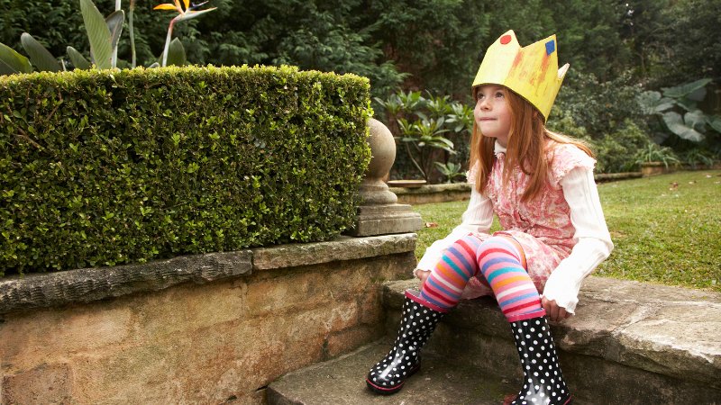 Ein Mädchen sitzt im Garten auf einer Stufe und hat eine Krone aus Papier auf dem Kopf.