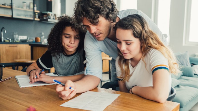 Ein Vater hilft seinem Sohn und seiner Tochter bei den Hausaufgaben.