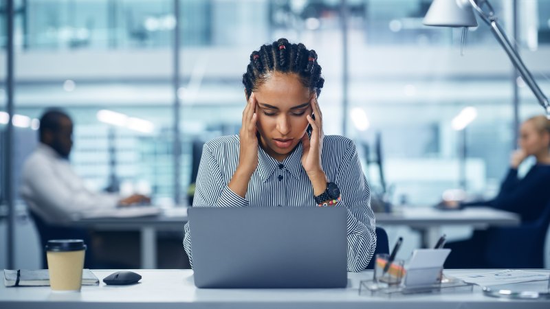 Gestresste, junge Büroangestellte leidet am Schreibtisch unter Kopfschmerzen.